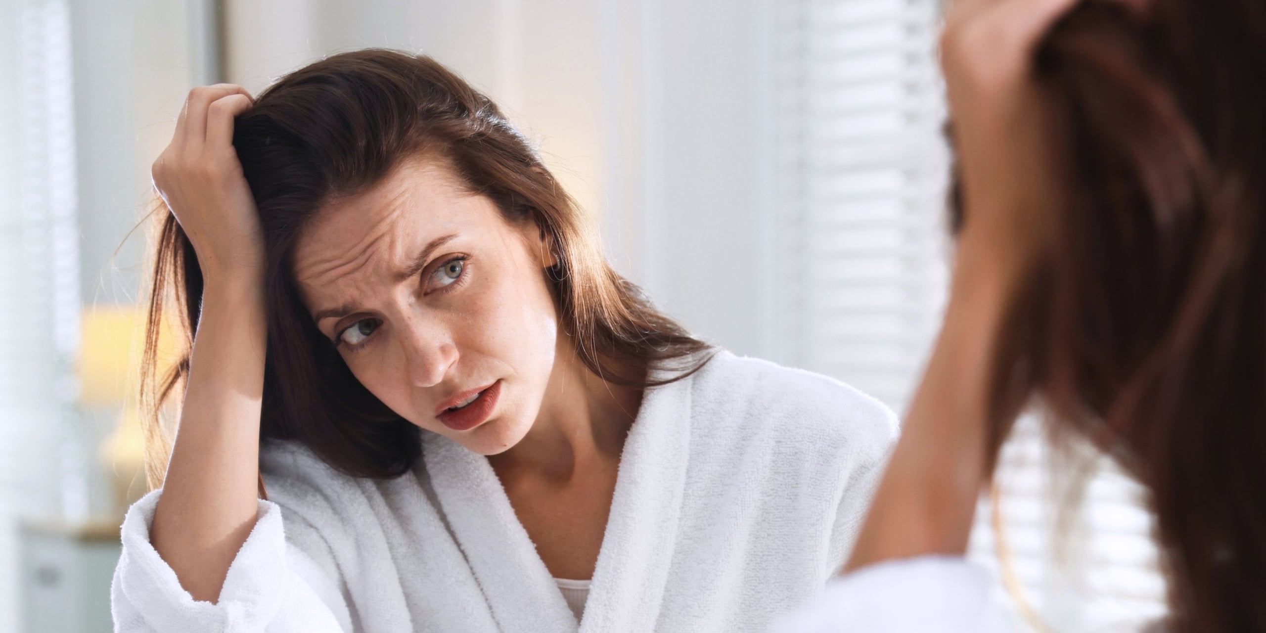 Woman looking at her hair loss pattern in the mirros